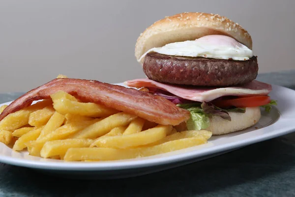 Homemade veal burger with bacon, cheese and fried egg with chips. isolated image