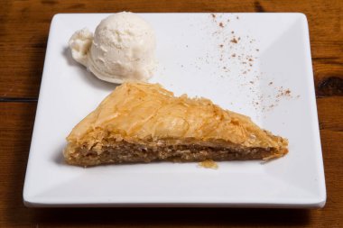 Geleneksel Arap tatlı baklavası. Beyaz tabakta ceviz, bal ve dondurma. Gri masa örtüsü manzaralı.