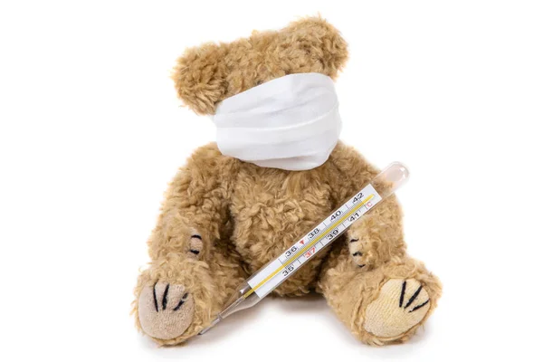 泰迪熊坐在那里 头戴医用口罩 头戴温度计 背景是白色的 呆在家里 照顾好孩子 — 图库照片