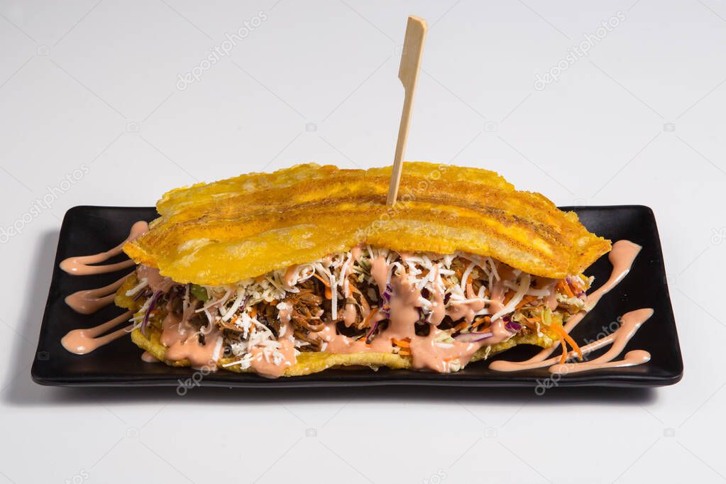 COLOMBIAN CARIBBEAN CENTRAL AMERICAN FOOD. Patacon or toston, fried and flattened whole green plantain banana on white plate with tomato sauce and chicharron white background