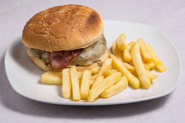 Sebzeli taze hamburger, beyaz tabakta patates kızartmasıyla servis ediliyor..