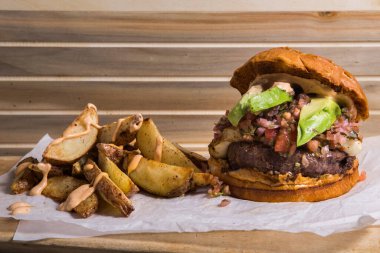 Avokado ile taze hamburger, ahşap arka planda patates kızartması ile servis edilir..