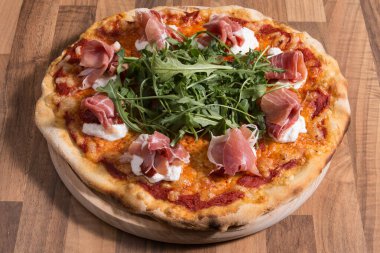 Jambonlu pizza, roka ve ahşap zeminde domates..