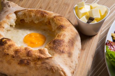 Ahşap bir masada peynirli yumurta ve Adjara Khachapuri.