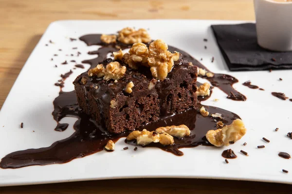 Chocolate vegan brownie cake with nuts and ice cream. White plate.