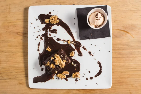 Chocolate vegan brownie cake with nuts and ice cream. White plate.