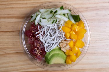 Şeffaf bir kasede mango, ton balığı, avokado, gula ve salatalıkla dürt.