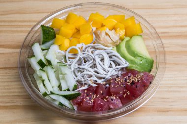 Şeffaf bir kasede mango, ton balığı, avokado, gula ve salatalıkla dürt.