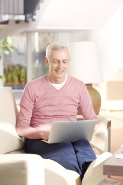 Evde dizüstü bilgisayar kullanan kıdemli adam.