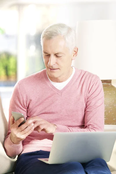 Senior man met laptop en mobiele telefoon — Stockfoto