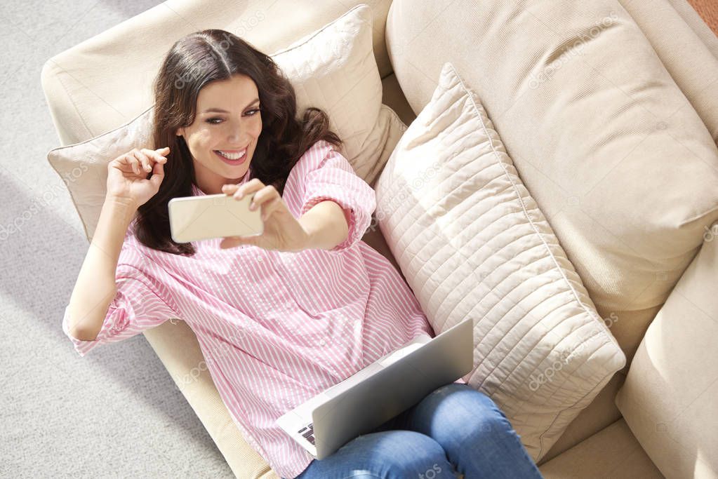 Woman taking selfie while relaxing on sofa