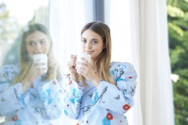 Bir fincan kahve duran bir pencere tarafından güzel gülümseyen genç kadının.