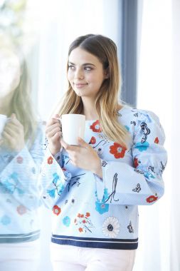 Bir fincan kahve duran bir pencere tarafından güzel gülümseyen genç kadının.