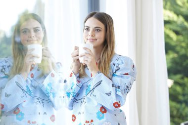 Bir fincan kahve duran bir pencere tarafından güzel gülümseyen genç kadının.