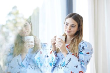 Bir fincan kahve duran bir pencere tarafından güzel gülümseyen genç kadının.