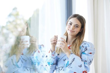 Bir fincan kahve duran bir pencere tarafından güzel gülümseyen genç kadının.