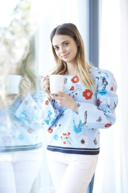 Bir fincan kahve duran bir pencere tarafından güzel gülümseyen genç kadının.