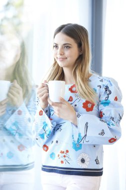 Düşünceli pencereden bakarak ve evde çay içme güzel genç kadın.