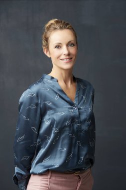 Koyu arka plan ayakta ve kameraya bakarak güzel gülümseyen Olgun kadın.