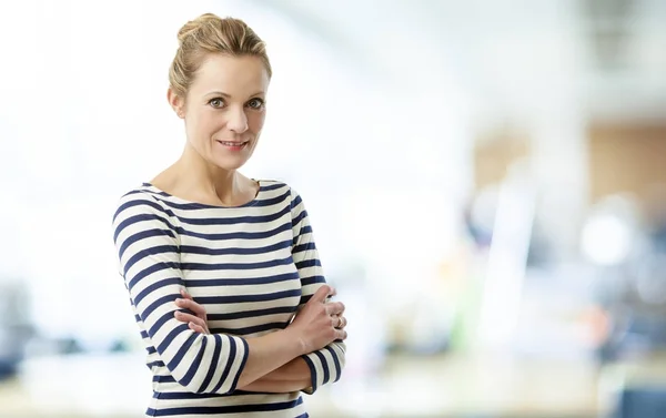 Smiling middle aged sales manager woman standing with arms crossed in office.