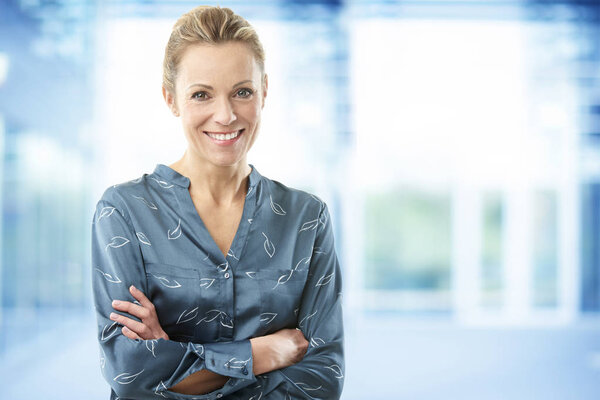 Smiling middle aged financial assistant woman standing with arms crossed in office. 