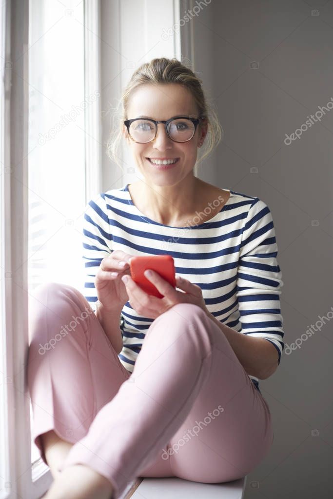 Happy casual woman using her mobile phone and text messaging while relaxing at home.