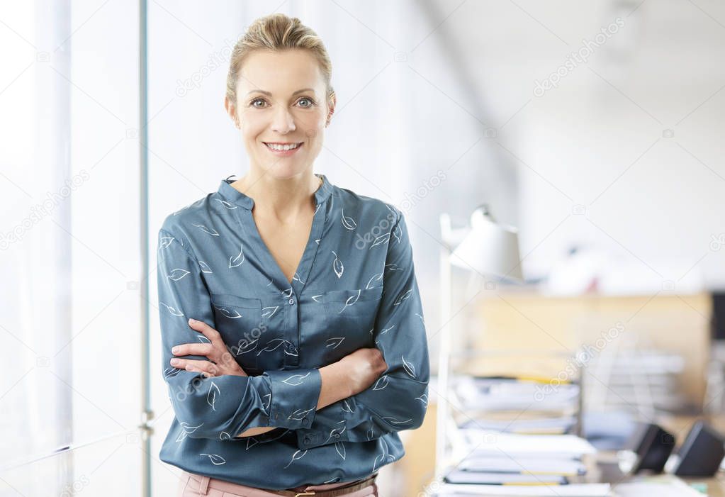 Confident smiling financial advisor businesswoman standing with arms crossed at the office. 