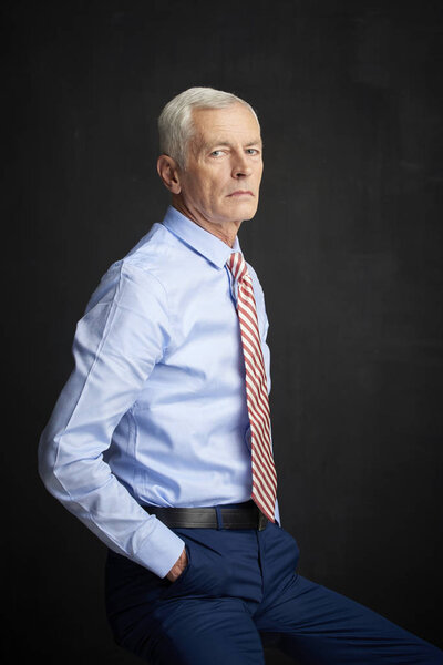 Executive senior man wearing shirt and tie sitting at black wall
