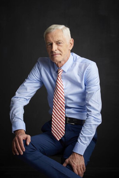 Executive senior man wearing shirt and tie sitting at black wall