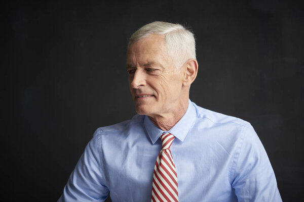 Frowning senior man wearing shirt and tie on dark wall. 