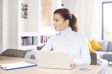 Süre masa başında oturan ve evden çalışan dizüstü bilgisayar ve cep telefonu kullanan güzel orta yaşlı kadın. Ev ofis. 