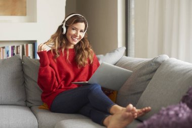 Tam uzunlukta atış olan kulaklık ve kanepede oturan ve müzik listeleme laptop çekici kadın.