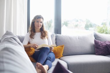 Güzel orta yaşlı kadın evde iyi bir kitap okurken thoughtfullly arıyor.