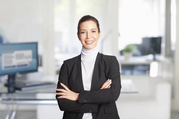 Smiling executive financial advisor businesswoman standing with arms crossed at the office.
