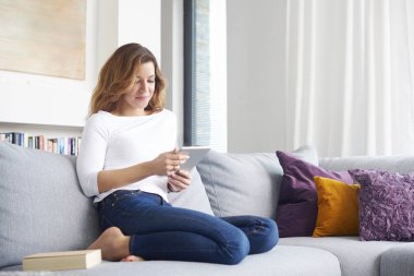 Orta gülümseyen yaşlı kadın kanepe evde dinlenirken dijital tablet kullanma.