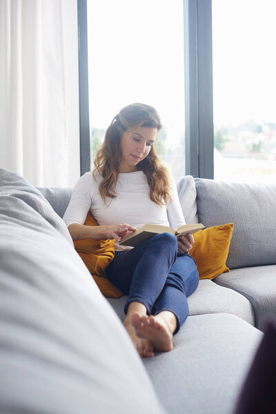 Beautiful middle aged woman looking thoughtfullly while reading a good book at home.