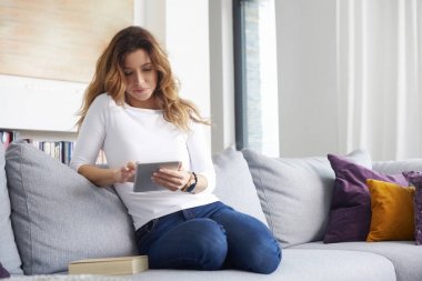 Orta gülümseyen yaşlı kadın kanepe evde dinlenirken dijital tablet kullanma.