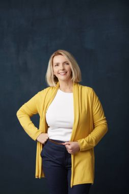 Güzel yaşlı kadın giyiyor rahat kıyafetler gülümseyen ve kamera, koyu arka plan dururken bakarak.