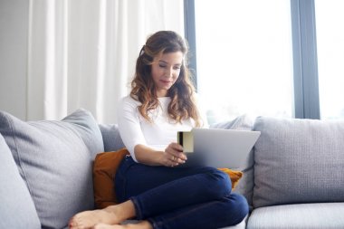 Olgun kadın yaşam kanepe olmadan evden alışveriş yaparken laptop ve banka kartını kullanarak.