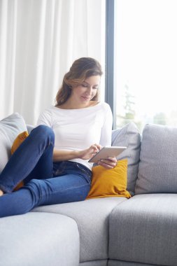 Orta gülümseyen yaşlı kadın kanepe evde dinlenirken dijital tablet kullanma.