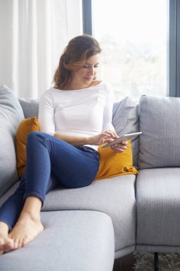 Orta gülümseyen yaşlı kadın kanepe evde dinlenirken dijital tablet kullanma.