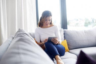 Orta yaşlı kadın evde kanepede dinlenirken dijital tablet kullanma.