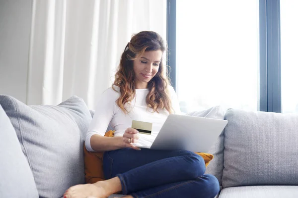 成熟的妇女使用膝上型电脑和她的银行卡 而没有活沙发在家购物 — 图库照片