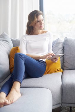 Orta yaşlı kadın düşünme olumlu düşünceler dijital tablet evde kullanırken. 