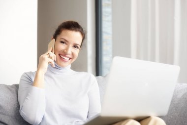 Cep telefonunu kullanarak ve laptop ve evden çalışan ile kanepede otururken arama yapma Olgun kadın. 