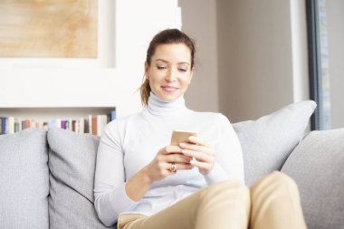 Esmer Olgun kadın kanepe ve onun cep telefonu mesajlaşma metin rahatlatıcı gülümseyen.