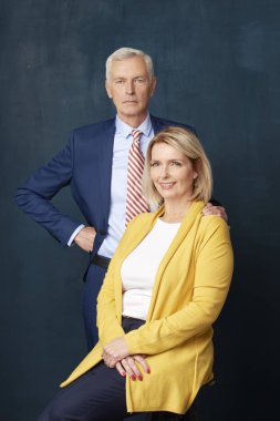 Zarif üst düzey çift. Güzel Olgun kadın kamera ve smling bakarak süre takım ayakta arkasında oturan ve yaşlı adam.