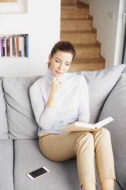Kanepe ve okuma kitabı evde oturan güzel gülümseyen Olgun kadın. 