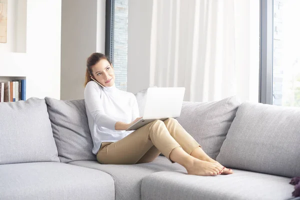 Full length shot of confident woman working from home. Beautiful female talking with somebody and manage her business while sitting sofa at home.