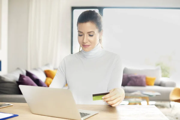 有吸引力的女人用她的笔记本电脑在家里坐在办公桌前用她的信用卡进行网上购物 — 图库照片